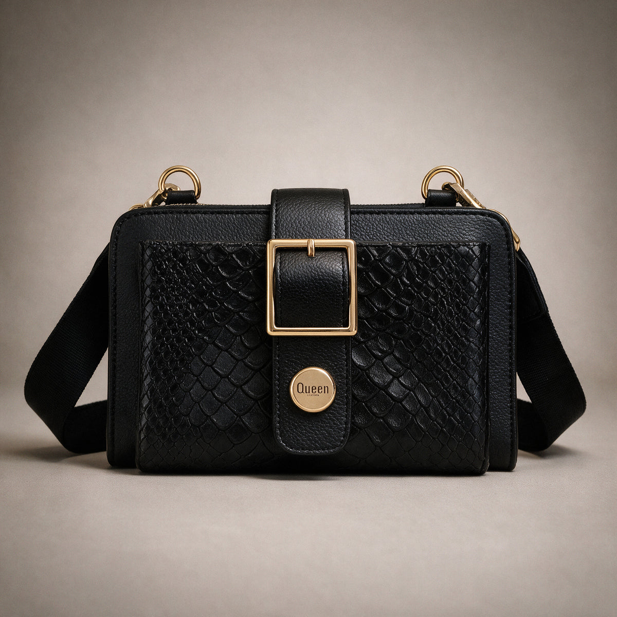 Bolso Charlotte Negro Luxury visto de frente sobre fondo greige de estudio, con hebilla dorada y correa ancha de tela