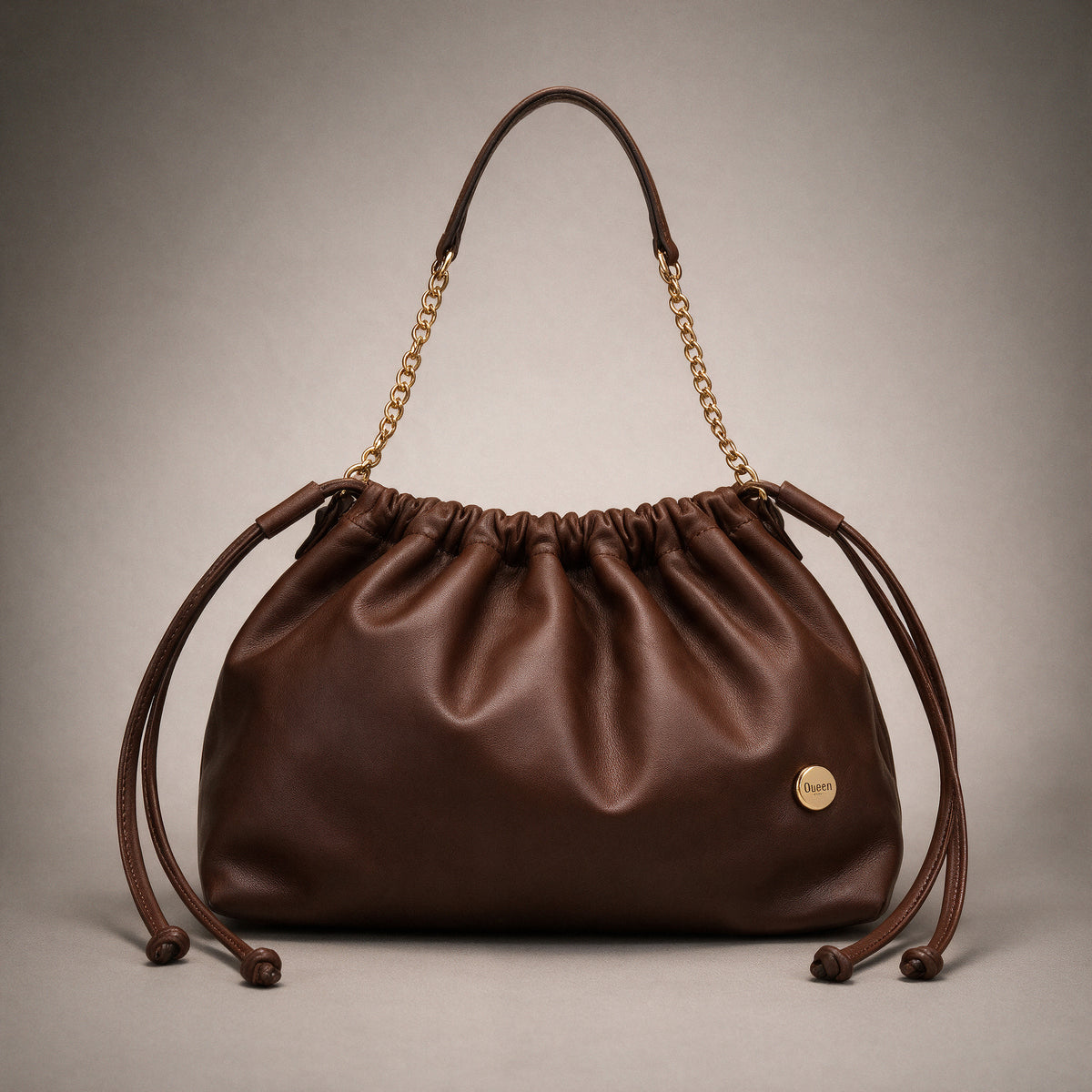 Bolso Mia en cuero chocolate mate visto de frente sobre fondo greige de estudio, con cadena dorada y cordones de cuero