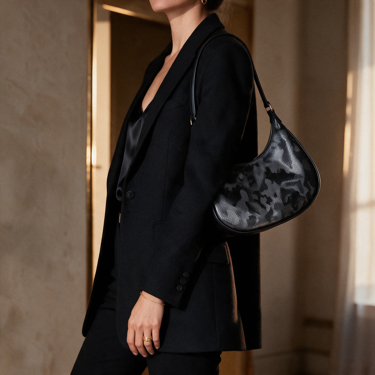 Bolso Roissy Negro Luxury bajo el brazo de una mujer con blazer negro sastre y camisola de seda, en un interior de yeso con luz dorada