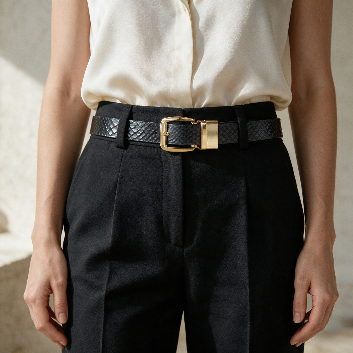 Cinturón Dama Luxury Negro con hebilla dorada, puesto sobre pantalón negro de talle alto y blusa de seda marfil